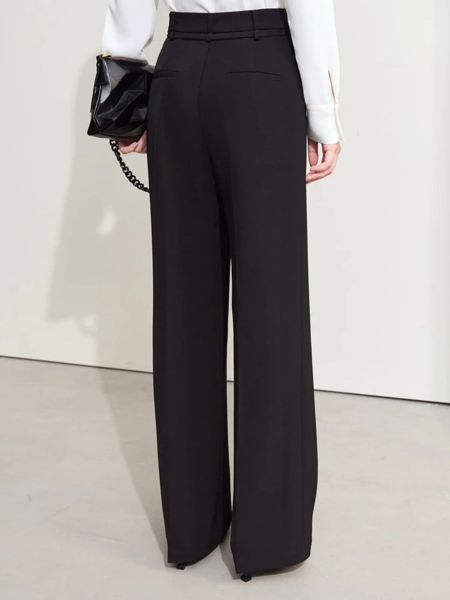 Side-back angle of black trousers with soft drape and ankle-length hem