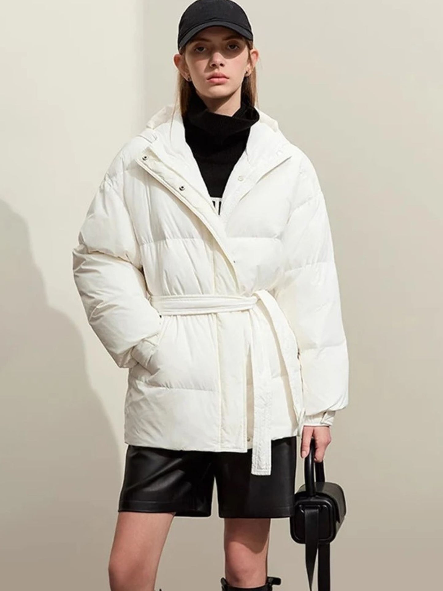 White belted puffer jacket worn with cap and crossbody bag, zip partially open.