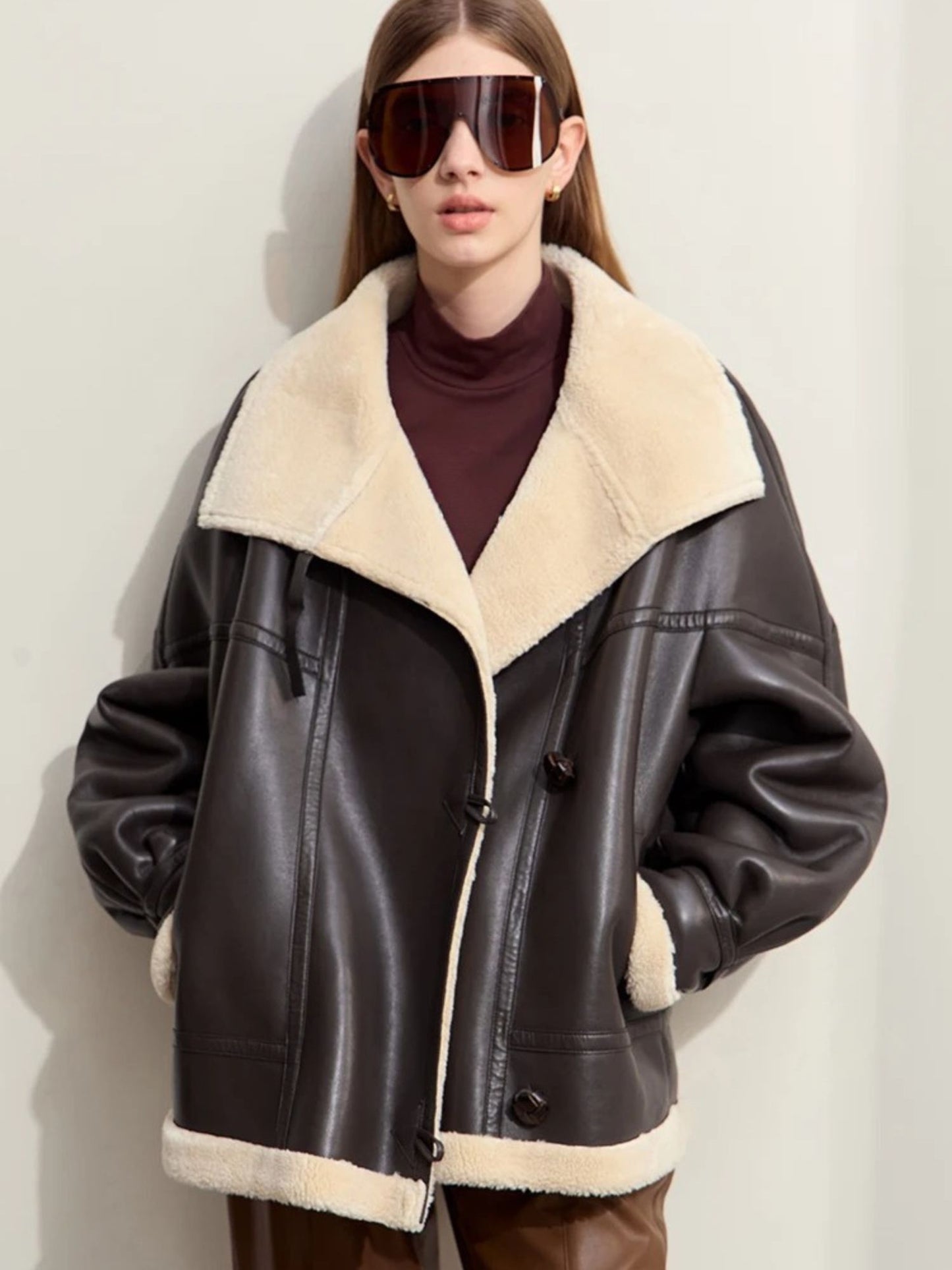 Person wearing a brown leather jacket with white fur lining against a plain background