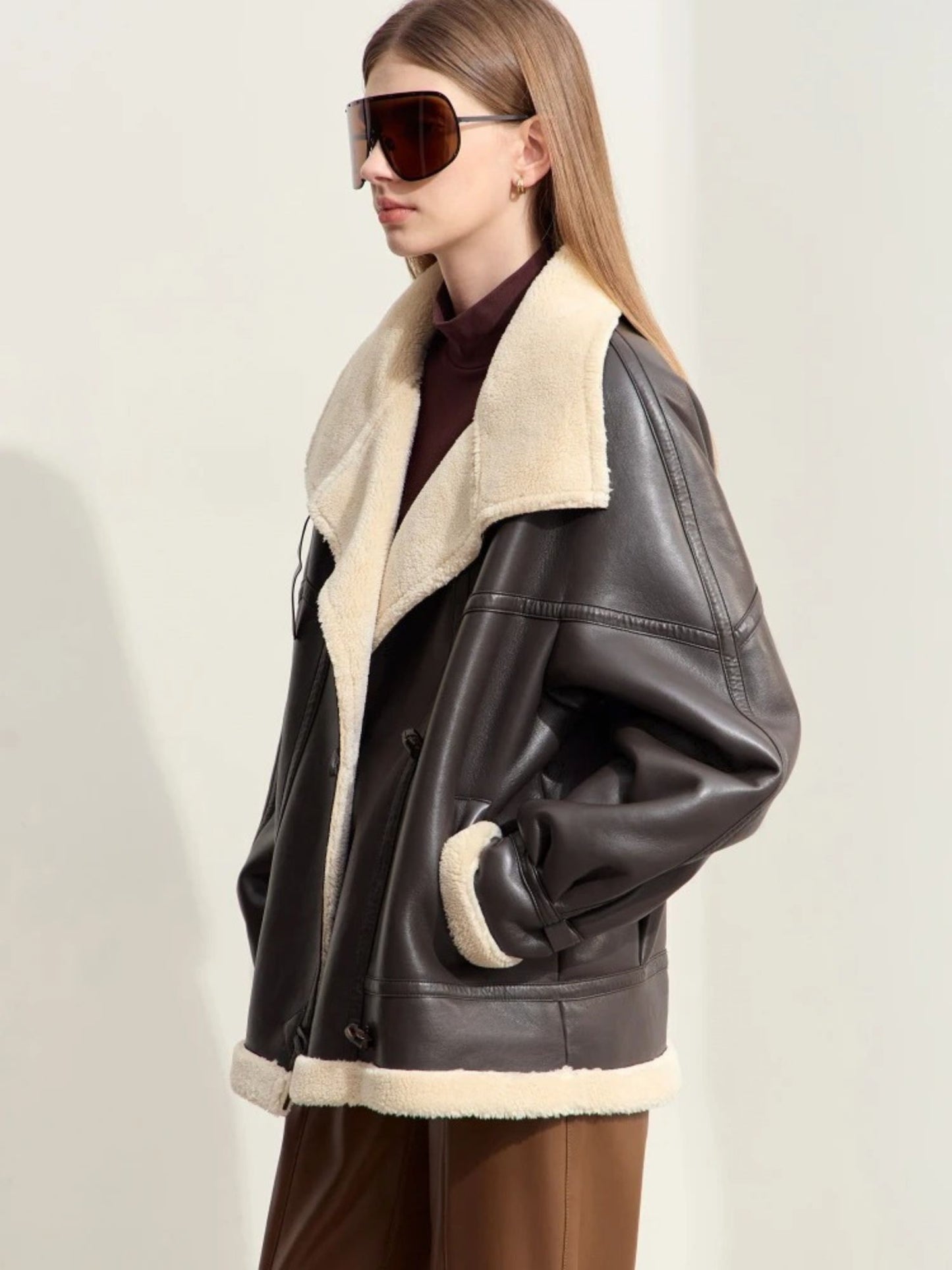 Person wearing a black leather jacket with beige interior and sunglasses on a light background