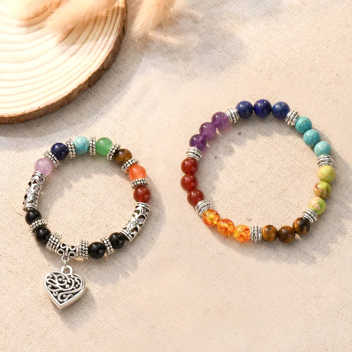 Colorful beaded bracelet one with a heart pendant on a plain canvas and a plain wooden disc and a plant as decoration.