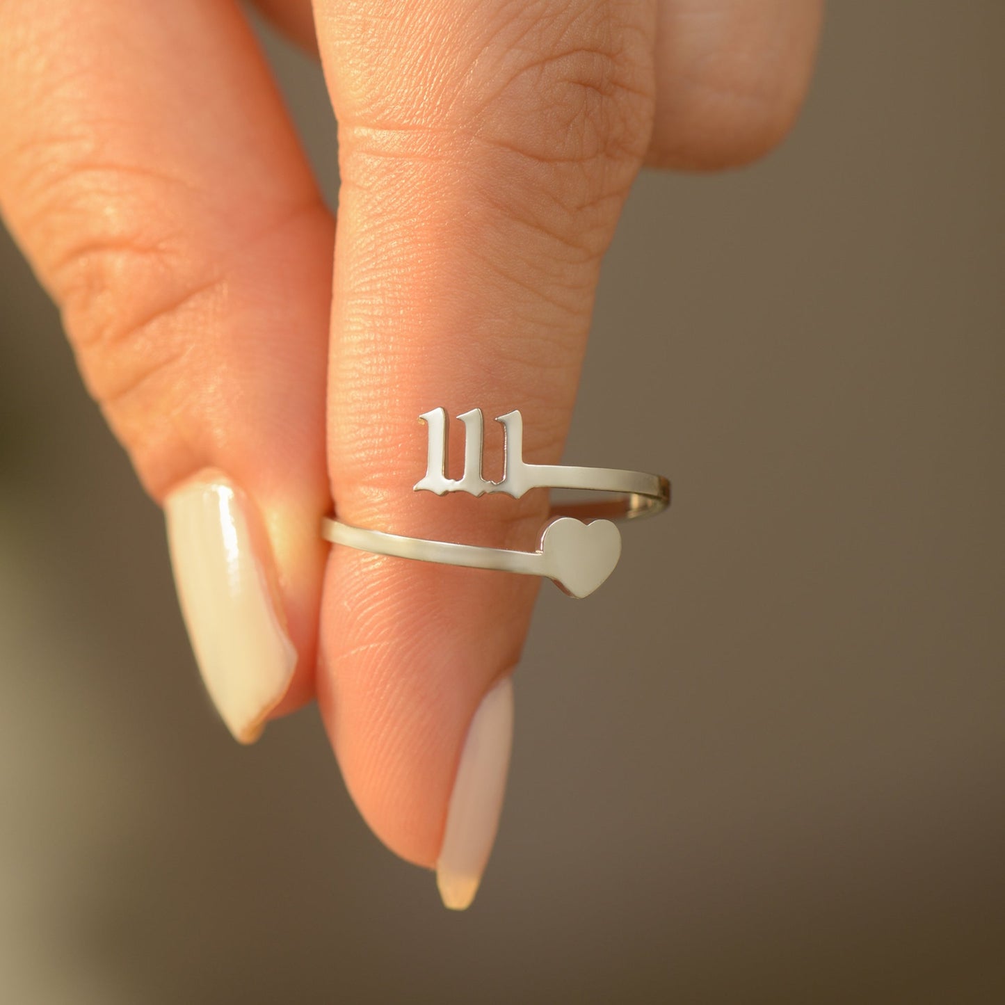 Silver ring with angel number 111 and heart charm on woman's fingers