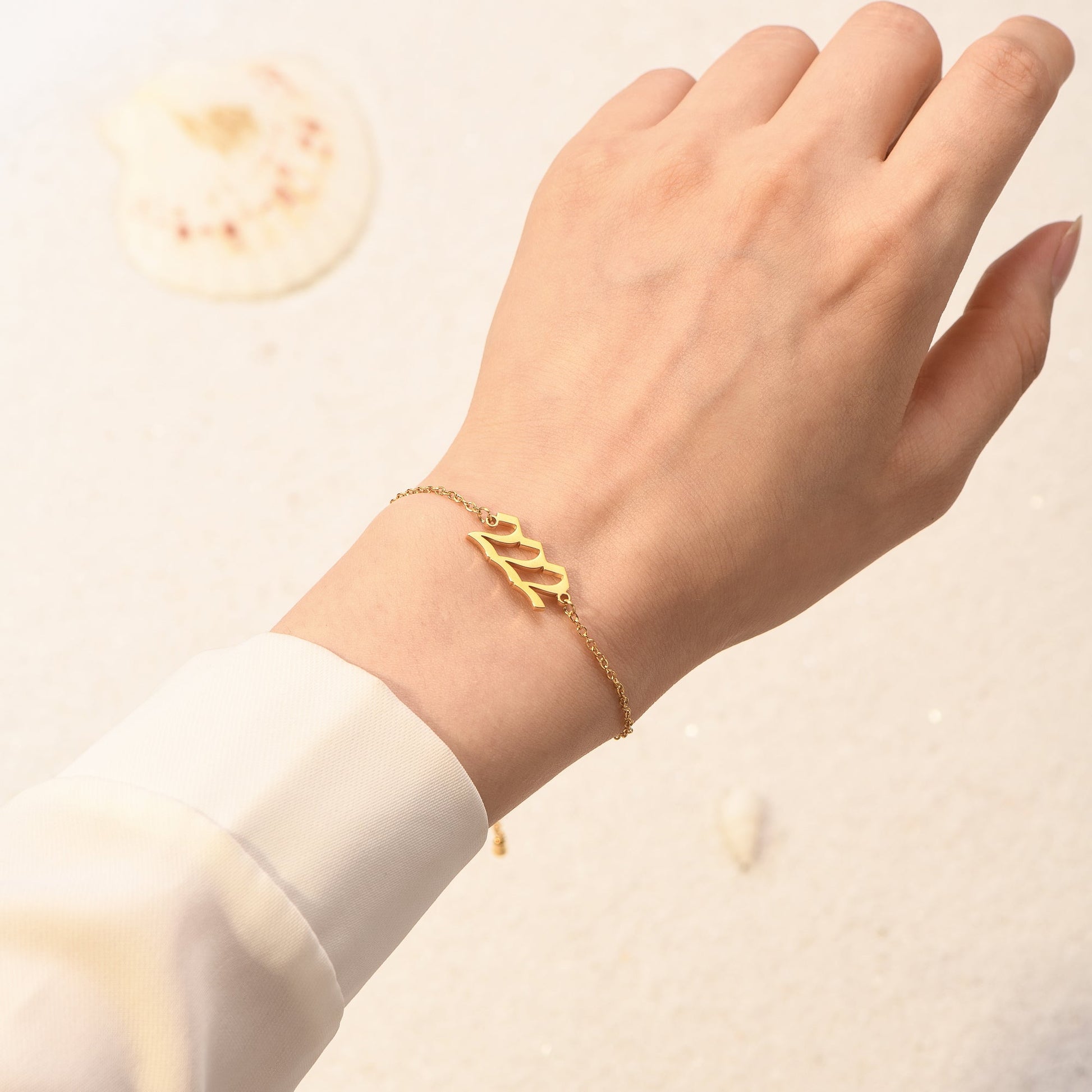 Gold angel number 222 bracelet on a woman's wrist wearing a white long sleeve in a light background