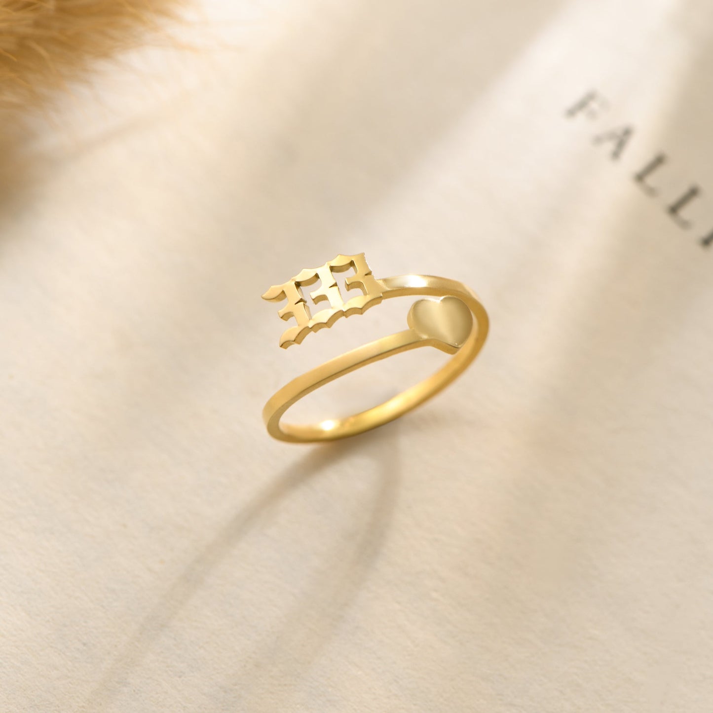 A gold ring with  angel number 333 and heart symbol on a bookpage.