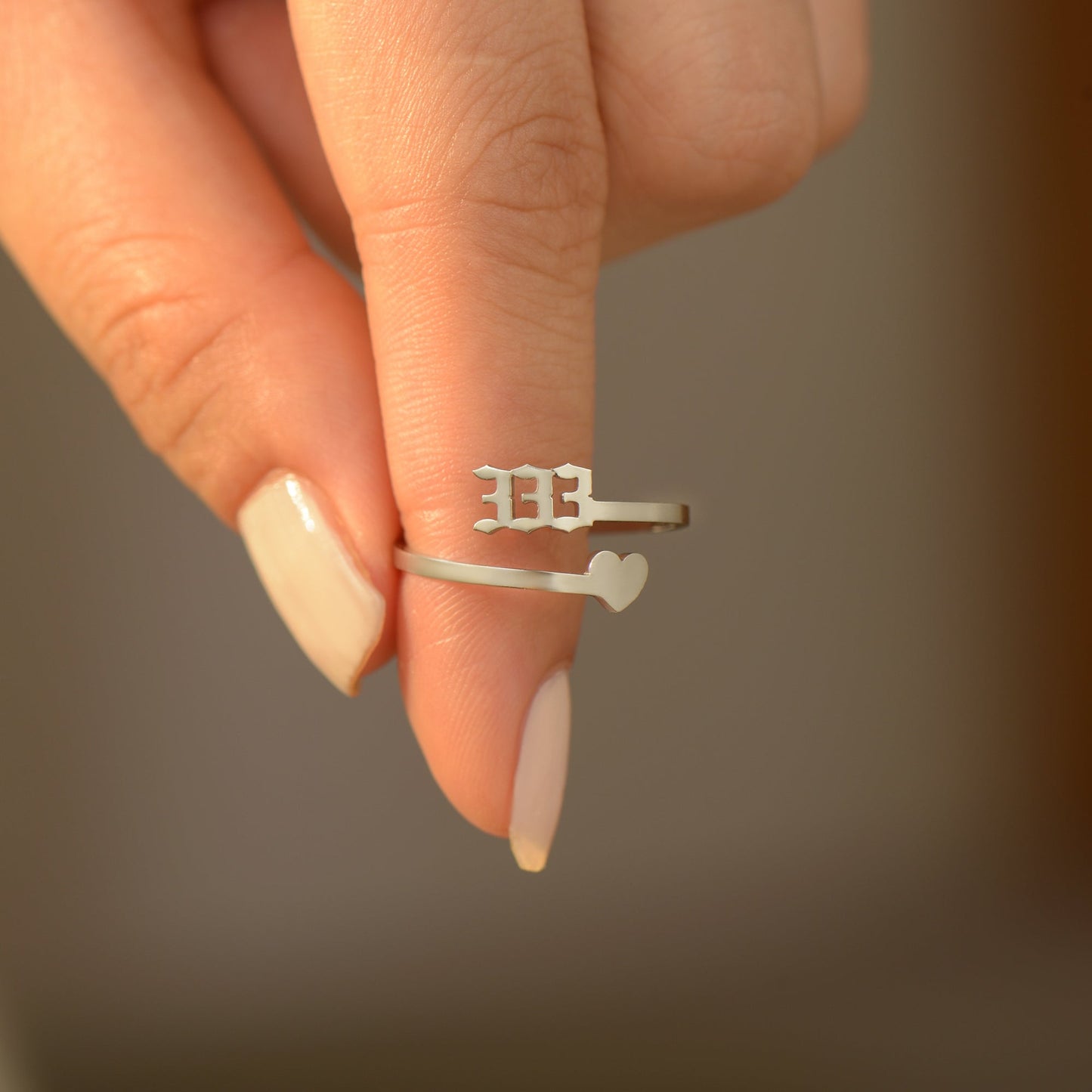 A woman holding a silver ring with angel number 333 and heart symbol