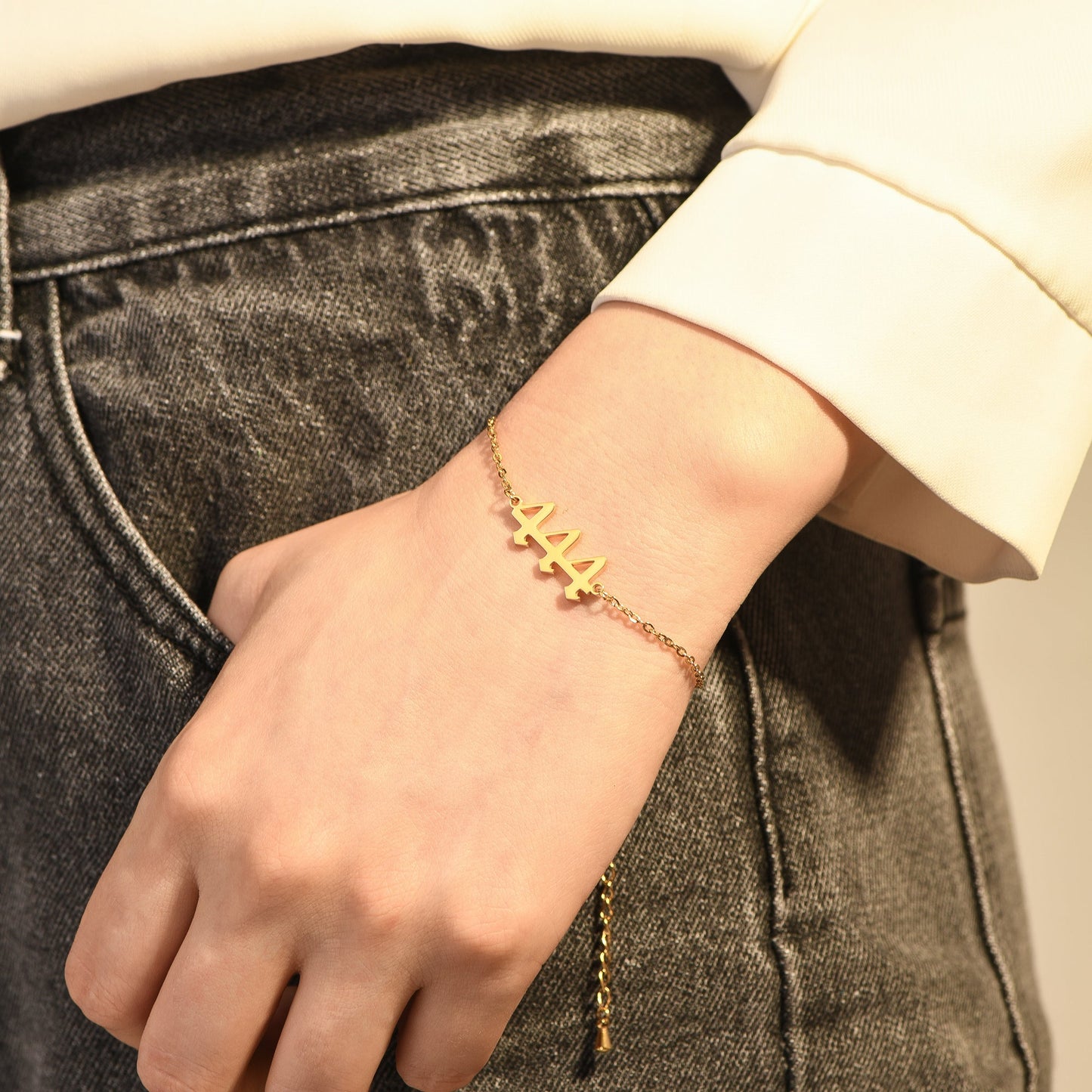 Gold bracelet with angel number 444 on a woman's wrist wearing a yellow long sleeve and black denim jeans