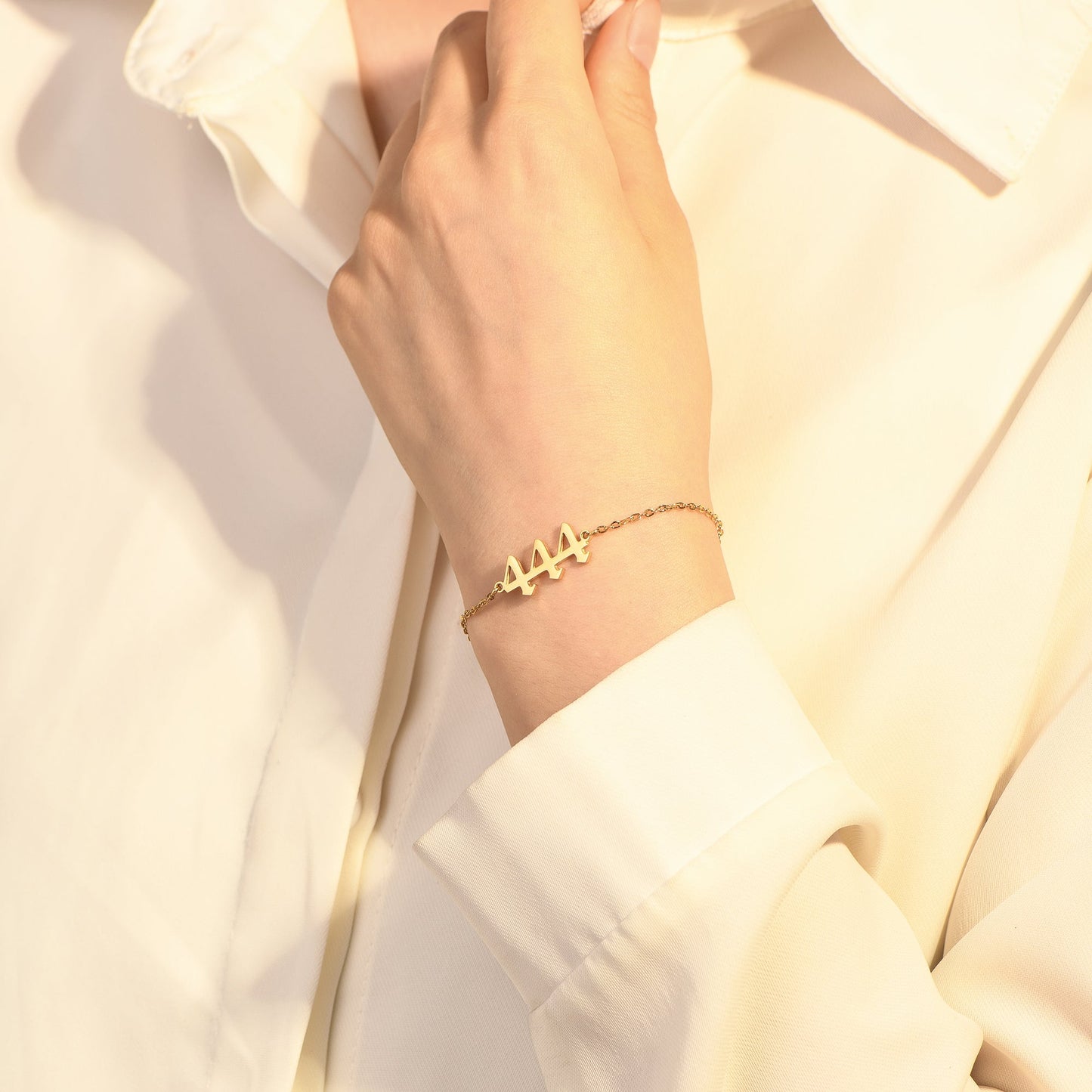 A gold bracelet with angel number 444 on a woman's wrist wearing a white long sleeve.