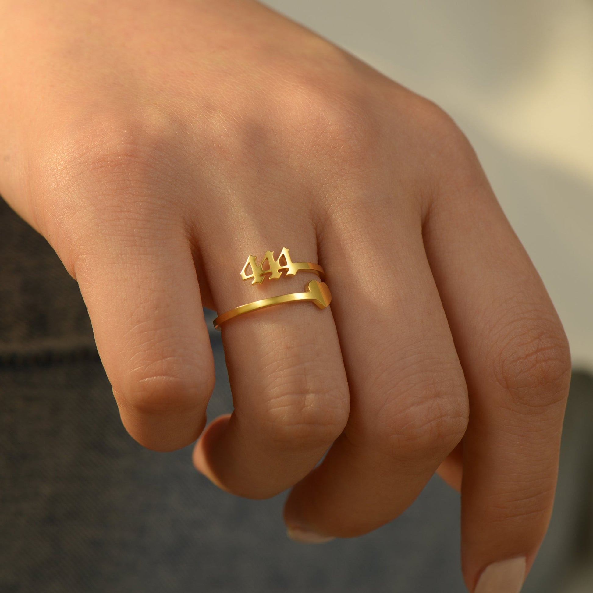 A woman wearing a gold ring with angel number 444 and a heart symbol 