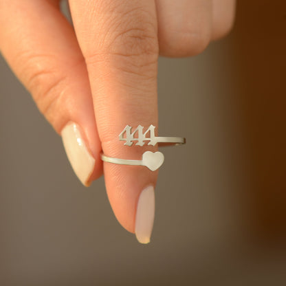 A silver ring with angel number 444 and a heart symbol on woman's finger.