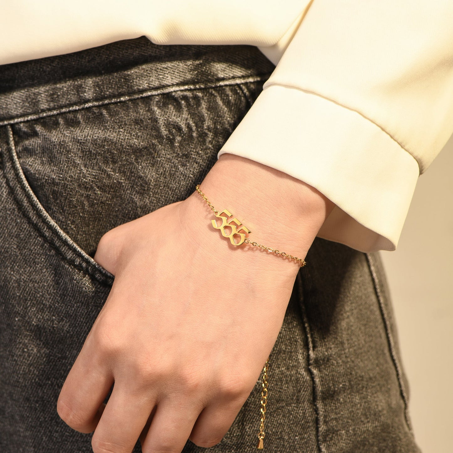 Gold bracelet with angel number 555 on woman's wrist who's wearing a yellow long sleeve and black denim