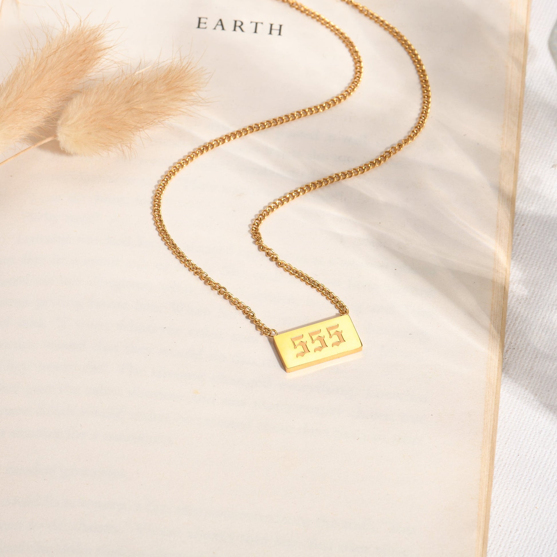 Gold chain necklace with gold angel number 555 pendant on a book page