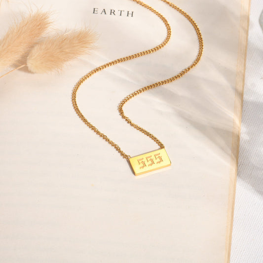 Gold chain necklace with gold angel number 555 pendant on a book page