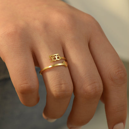 A gold ring with angel number 555 and a heart symbol on a woman's ring finger