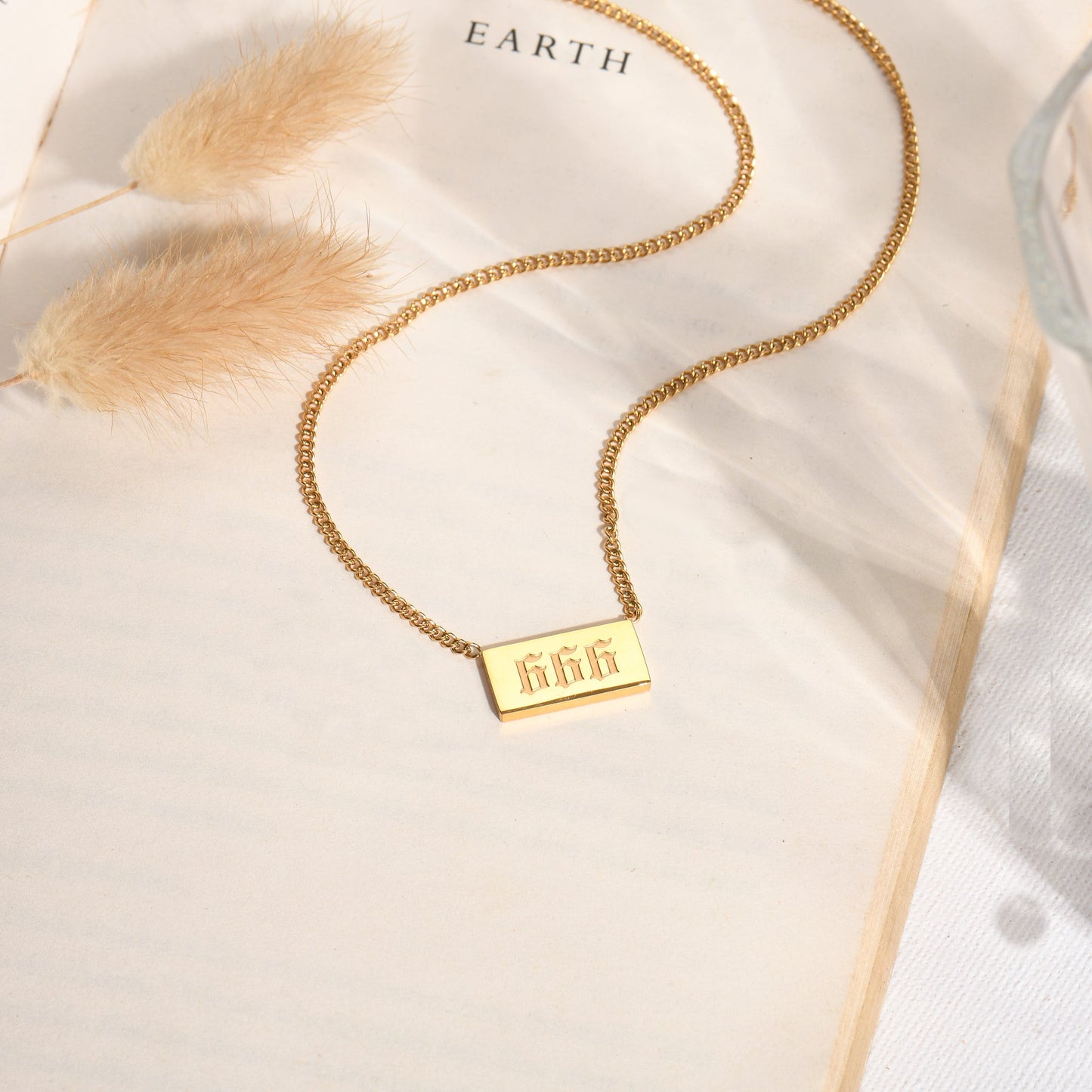 Gold chain necklace with gold angel number 666 pendant on a book page