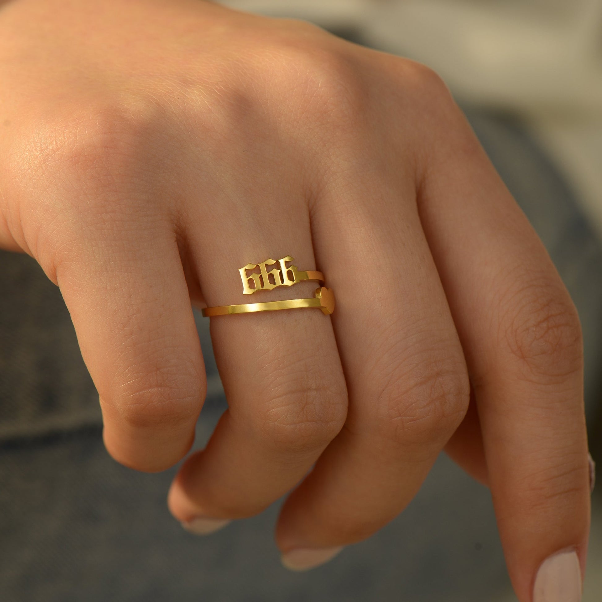 A gold ring with angel number 666 and  heart symbol on a woman's ring finger