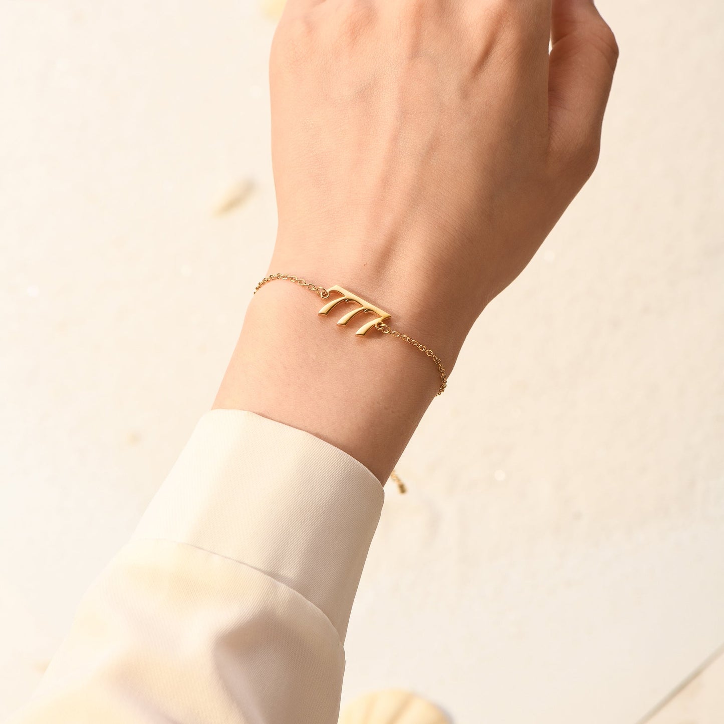 Gold bracelet with gold angel number 777 on woman's wrist