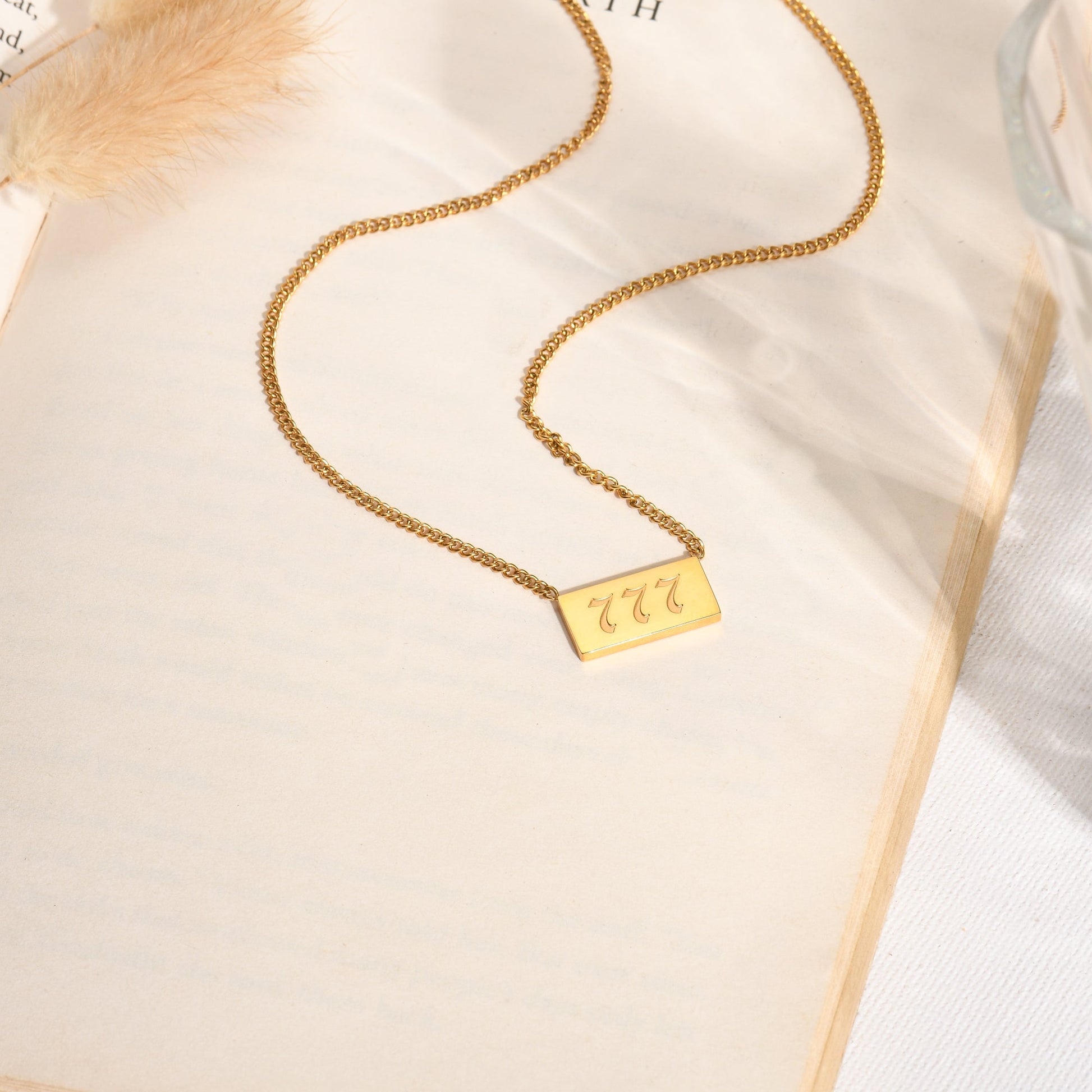 Gold chain necklace and gold angel number 777 pendant on a book page