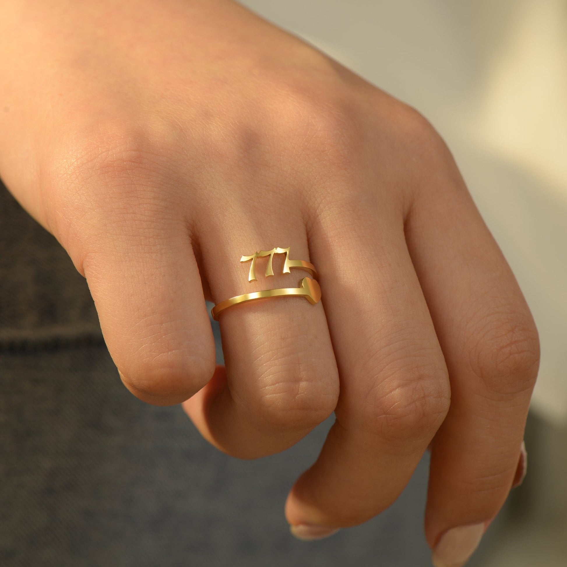 A gold ring with angel number 777 and heart symbol on a woman's ring finger