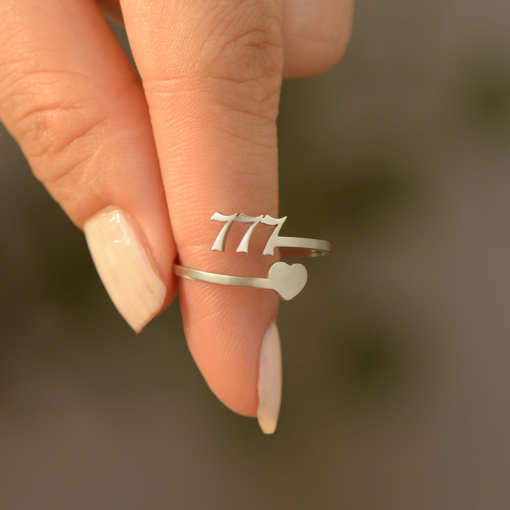 A silver ring with angel number 777 and heart symbol on a woman's finger