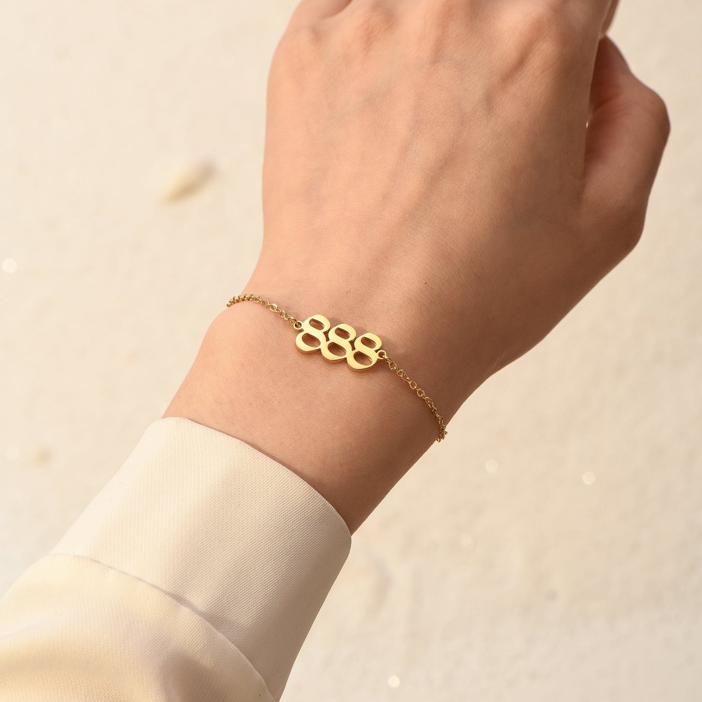 Gold chain bracelet with gold angel number 888 on woman's wrist