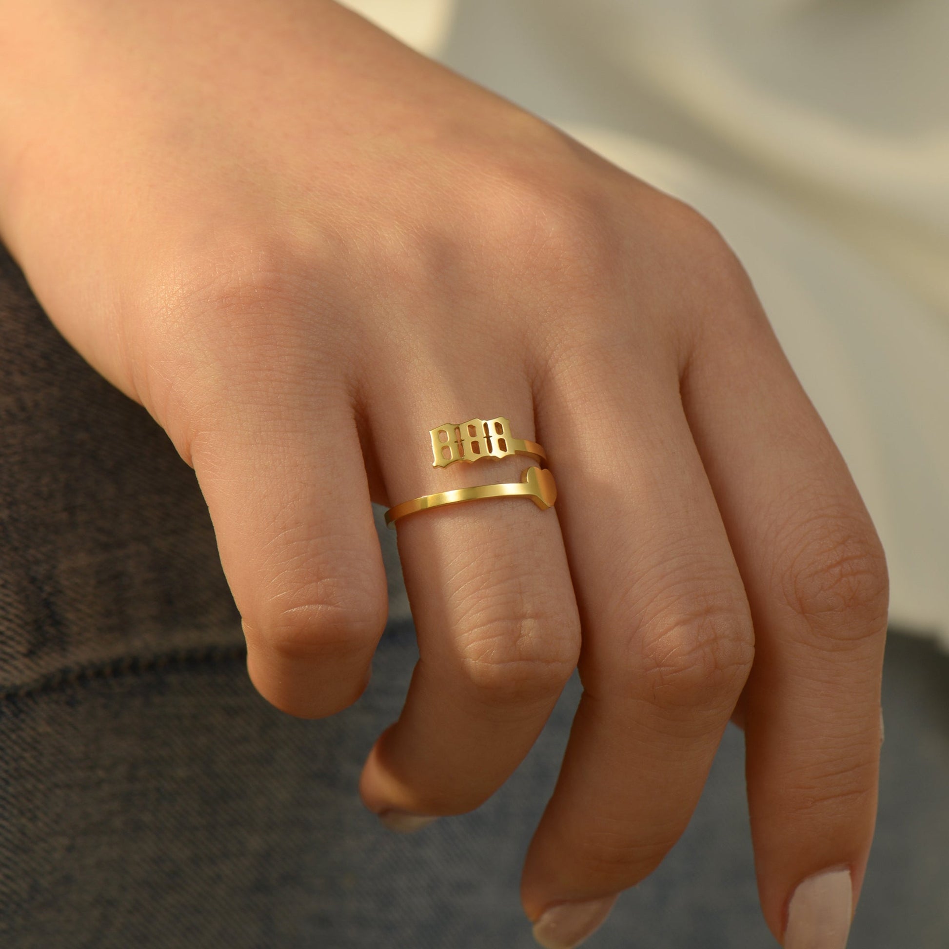 A gold ring with angel number 888 and a heart symbol on a woman's ring finger