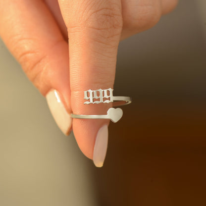 A silver ring with angel number 999 and heart symbol on a woman's finger