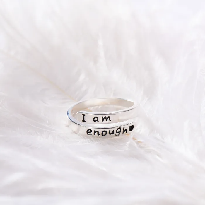 Silver ring with text engraving of "I am enough" on a white feather