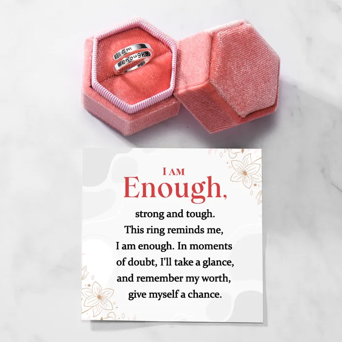 Silver ring with text engraving of "I am enough" inside a pink velvet ring box with an inspirational message card