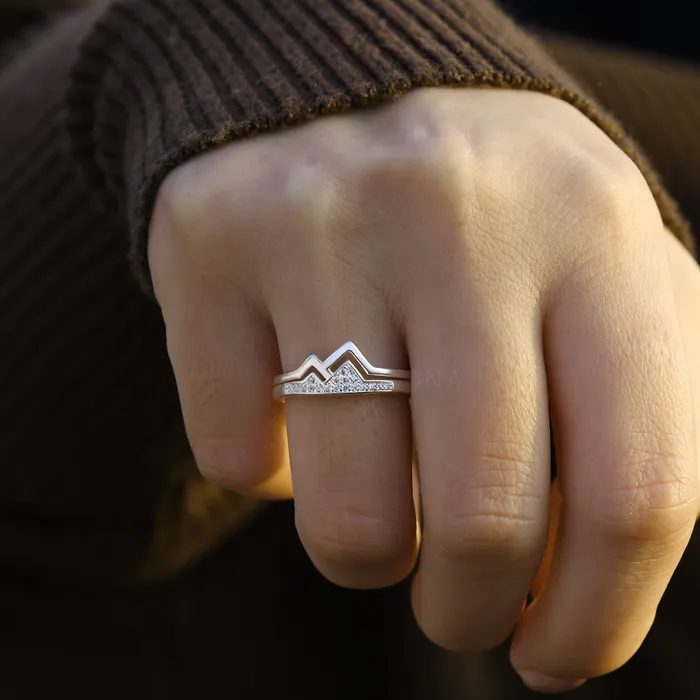 A female's hand wearing a silver mountain ring with stones on her ring finger.