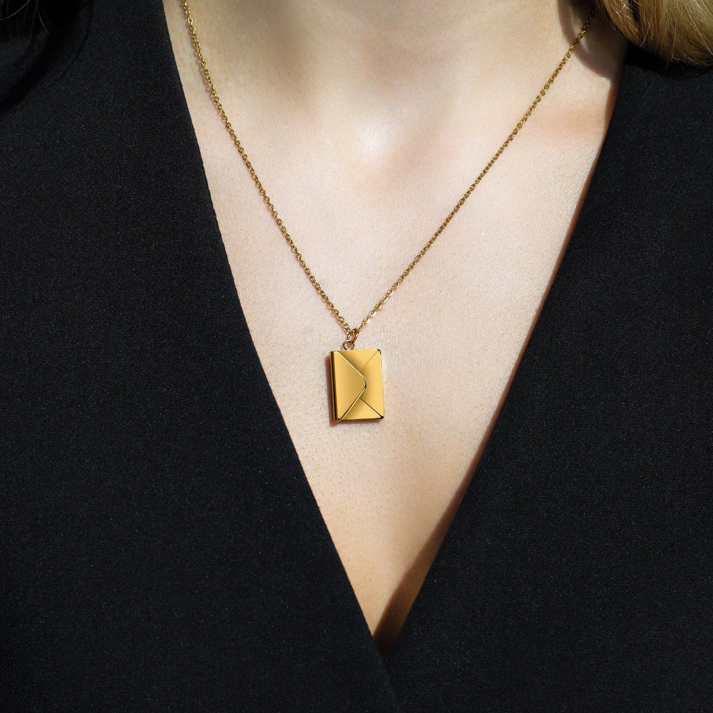 A woman wearing a gold chain necklace with an envelope-shaped pendant.