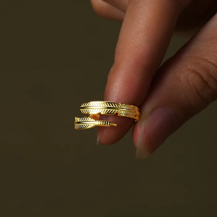 Gold feather-designed ring held by hand.