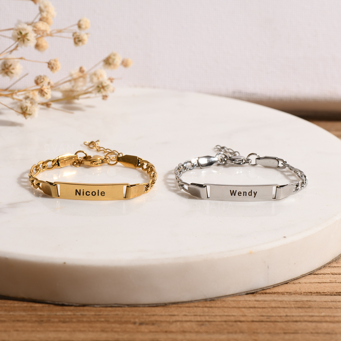 A silver and gold plated personalized name bracelet on a circular white disc with floral background