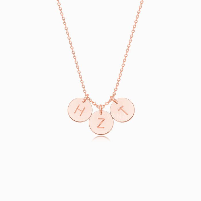 A rose gold necklace with three personalized initial discs on a white background