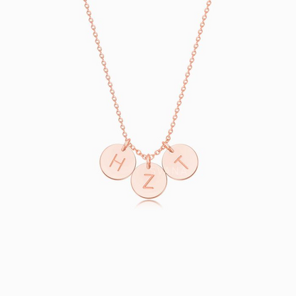 A rose gold necklace with three personalized initial discs on a white background