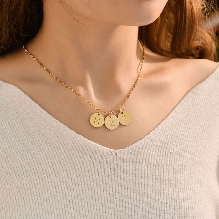 A gold necklace with three gold personalized initial discs on a woman