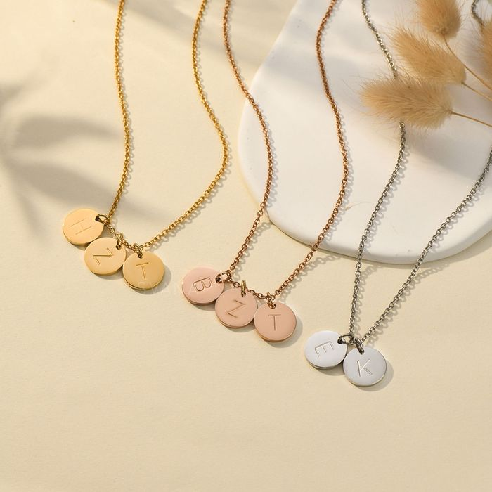 Gold, rose gold and silver necklaces with personalized initial discs on a plain canvas and floral background