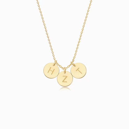 A gold necklace with three personalized initial gold discs on a white background