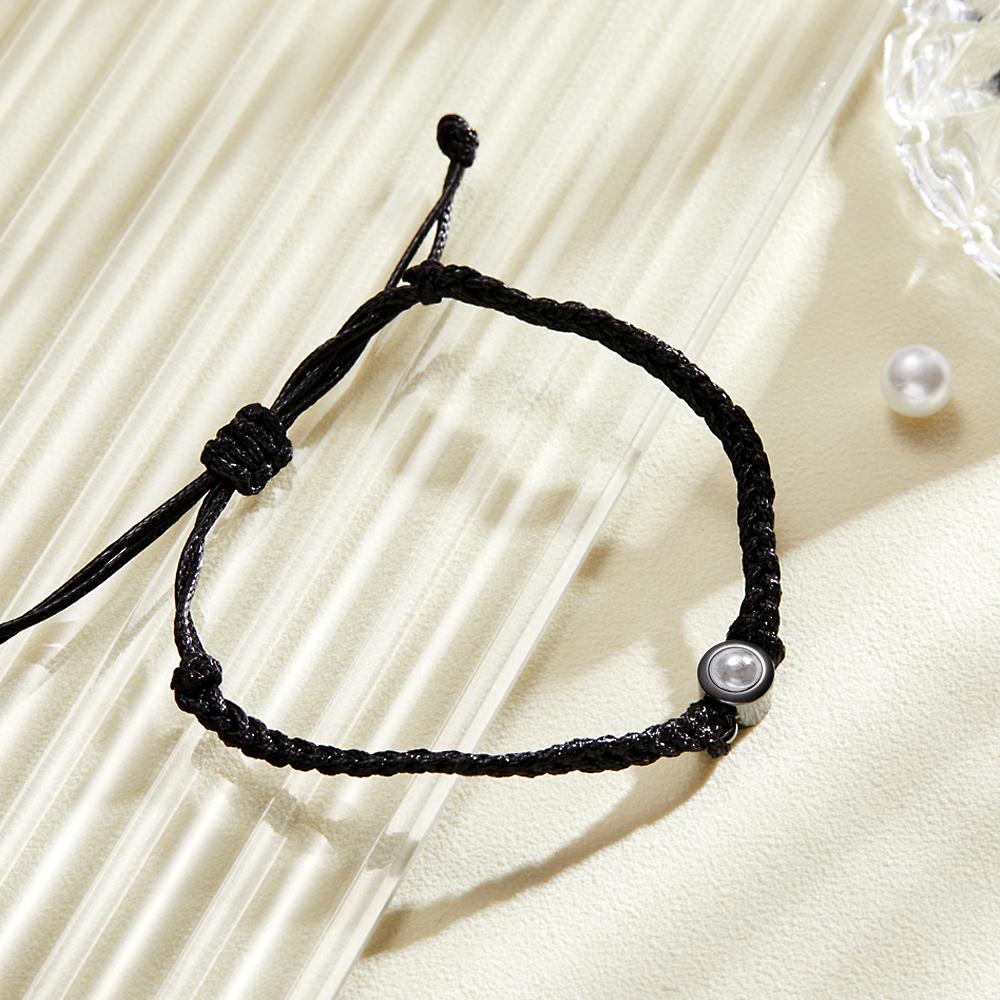 A lifestyle image of a black braided leather bracelet featuring a silver circular pendant designed to project an image