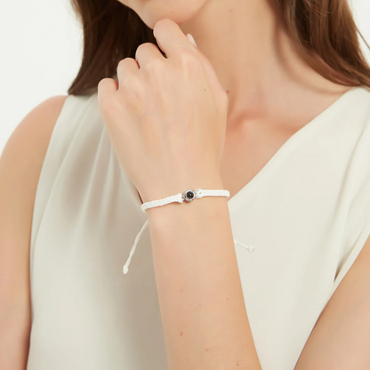 female in white top wearing a white circular pendant designed to project an image in a white background