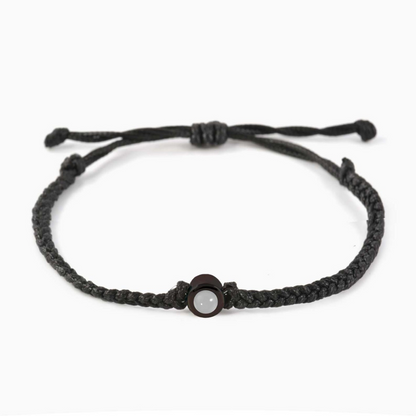 A black braided leather bracelet featuring a black circular pendant designed to project an image in a white background