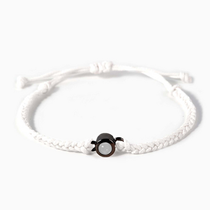 A white braided leather bracelet featuring a black circular pendant designed to project an image in a white background