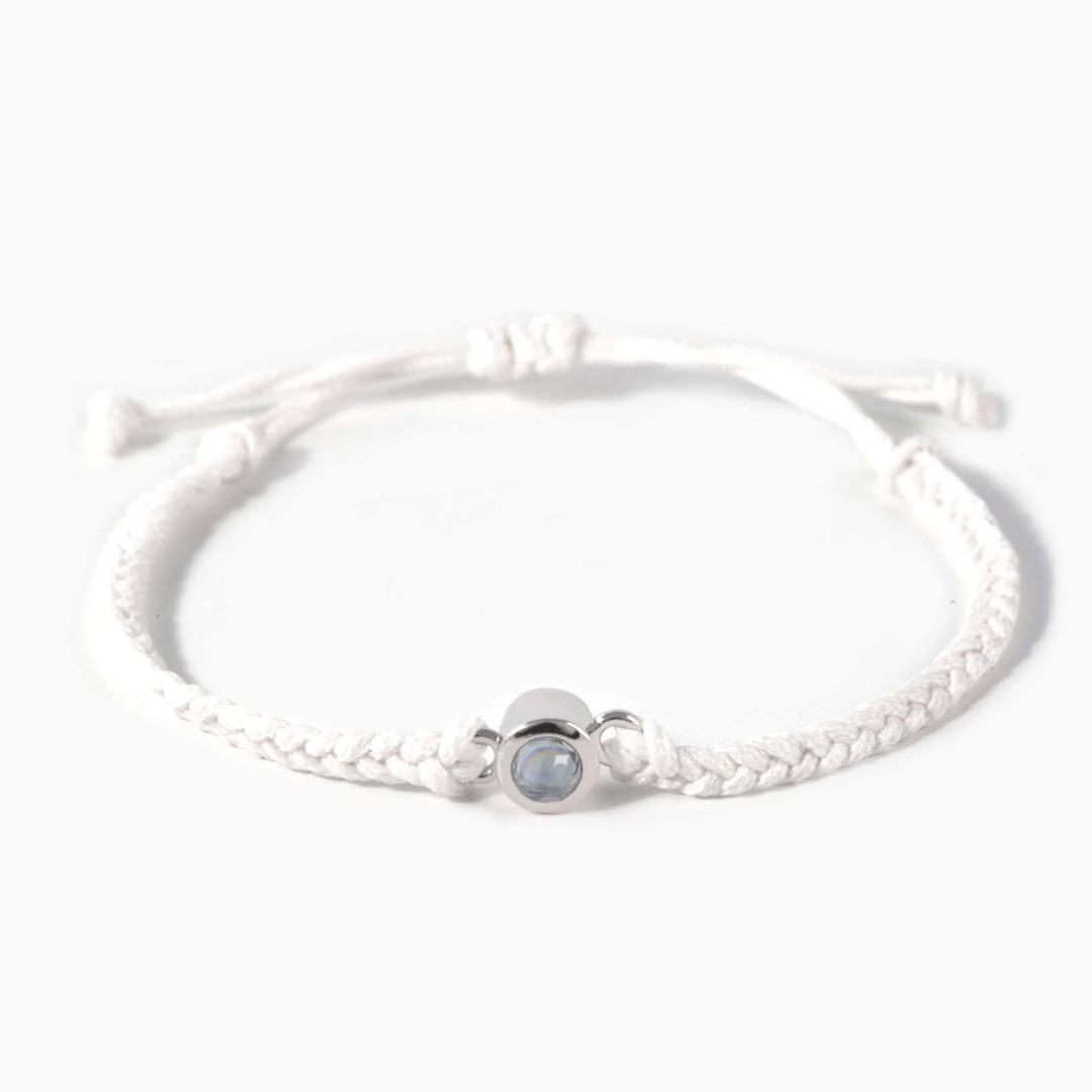 A white braided leather bracelet featuring a silver circular pendant designed to project an image in a white background