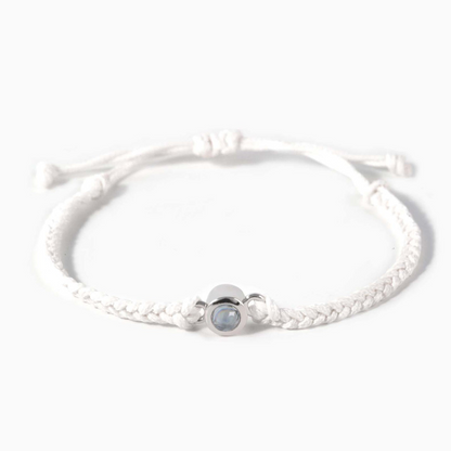 A white braided leather bracelet featuring a silver circular pendant designed to project an image in a white background