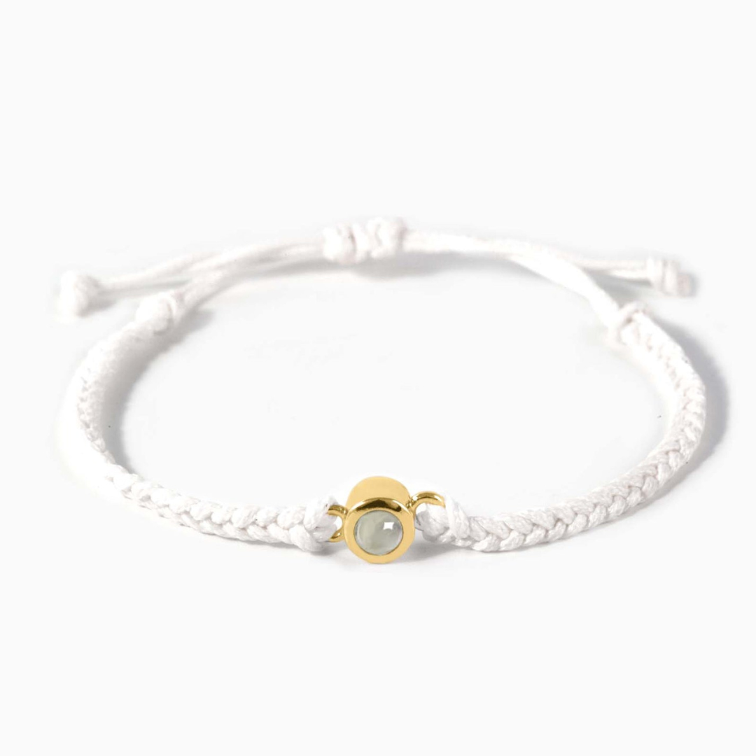 A white braided leather bracelet featuring a gold circular pendant designed to project an image in a white background