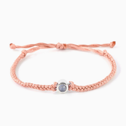 A peach pink braided leather bracelet featuring a silver circular pendant designed to project an image in a white background