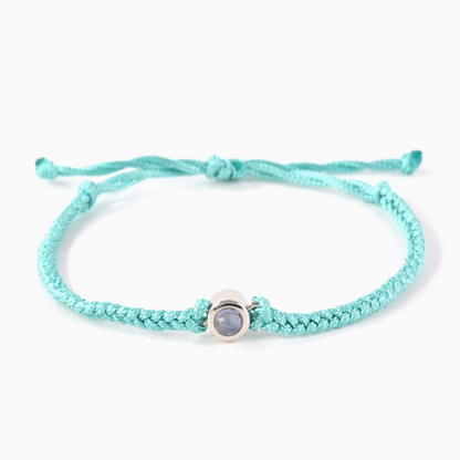 A turquoise braided leather bracelet featuring a silver circular pendant designed to project an image in a white background