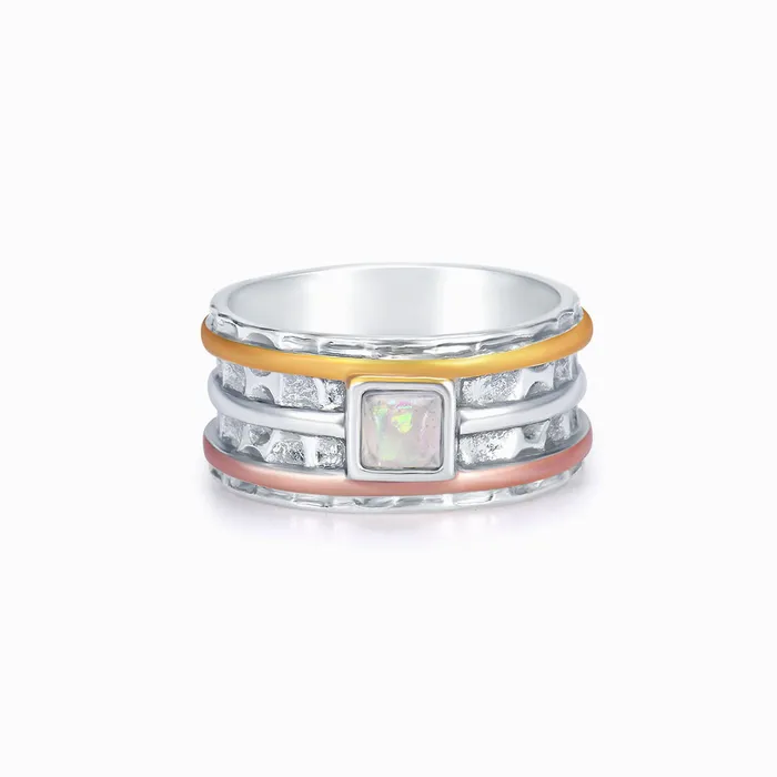 A silver ring with rose gold, silver, and orange bands surrounding it and a pearl-like square stone on a white background