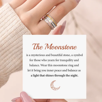 A silver ring with 3 bands and a pearl-like square stone on a woman's finger and an inspirational message card