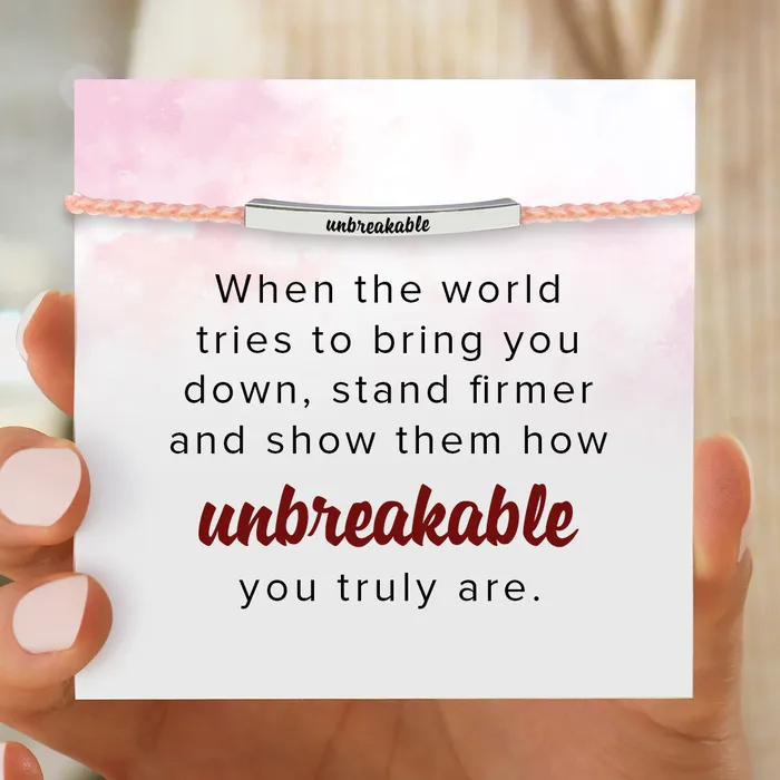 Pink bracelet with silver bar that has a text engraving "unbreakable" and an inspirational message card.