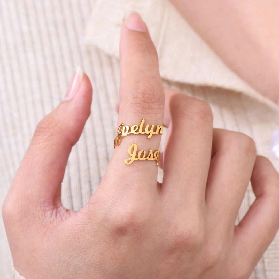 A gold ring featuring two names, "Evelyn" and "Jose," elegantly written in a cursive font. The names wrap around the finger, forming the band of the ring in a personalized, stylish design.